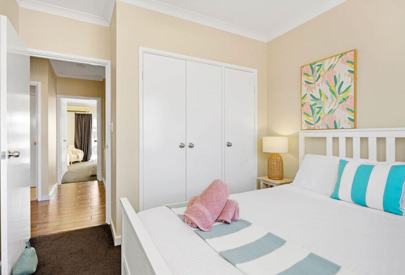 A hotel room with a bed, a wardrobe, a nightstand with a lamp, and a painting on the wall.