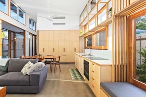 A compact kitchen with wooden cabinets, a dining area with a table and chairs, and a grey sofa.