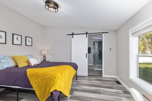 A bedroom with a bed, a yellow throw blanket, a bedside lamp, and framed artwork on the wall. - Lakefront Home with Dock, Firepit & Private Deck (Bloomingdale)