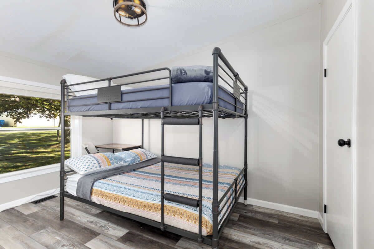 Un lit superposé avec une couvre-lit à motifs, une petite table et une vue sur la verdure à l’extérieur.
