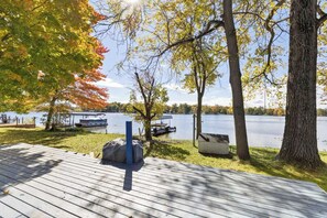 A wooden deck overlooking a lake with boats docked, surrounded by trees with autumn foliage. - Lakefront Home with Dock, Firepit & Private Deck (Bloomingdale)