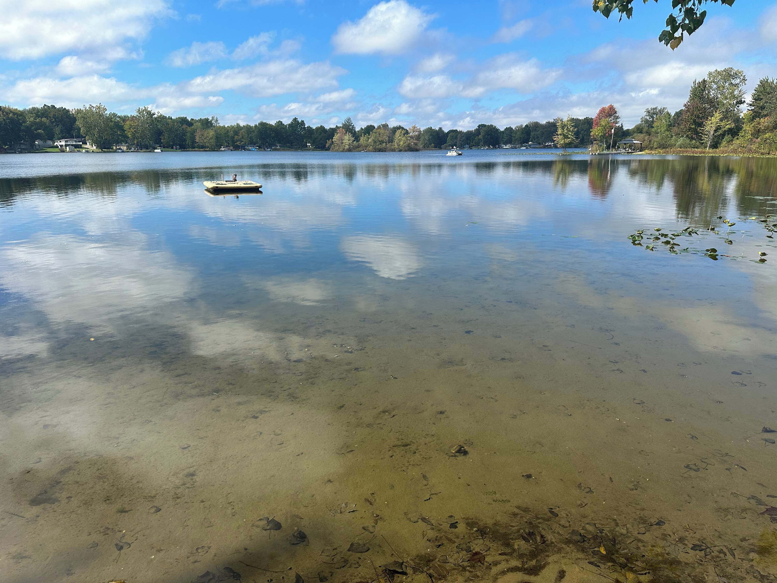 Un lac paisible avec une petite barque, une eau claire et une rive bordée d’arbres.