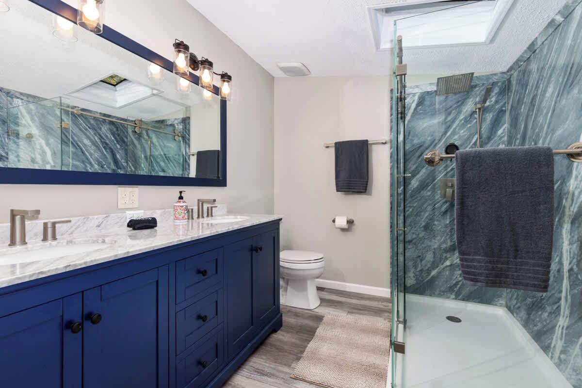 Une salle de bain moderne avec une douche à l’italienne en verre, un grand miroir et un pare-baignoire en marbre.