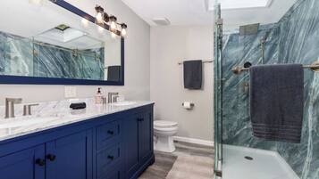 Une salle de bain moderne avec une douche à l’italienne en verre, un grand miroir et un pare-baignoire en marbre.