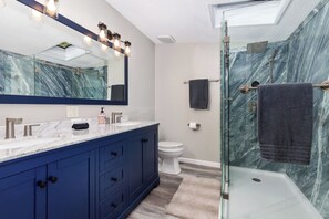 A modern bathroom with a glass shower enclosure, a large mirror, and a marble backsplash. - Lakefront Home with Dock, Firepit & Private Deck (Bloomingdale)