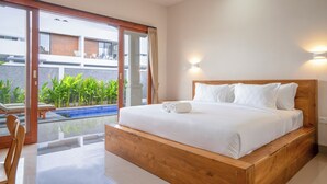A modern hotel room with a wooden bed, a glass door leading to a pool area, and a view of a building across the pool. - Aruna Villa 2 by Betterplace (Canggu)