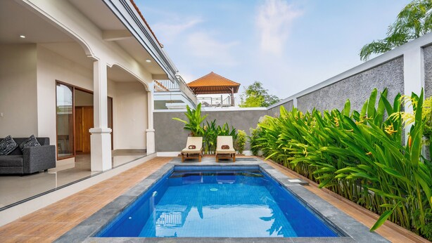 A modern swimming pool with two lounge chairs and a covered seating area, surrounded by lush greenery and a well-maintained patio. - Aruna Villa 2 by Betterplace (Canggu)