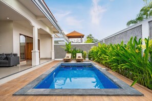 Ein moderner Pool mit zwei Liegestühlen und einer überdachten Sitzgruppe, umgeben von üppiger Bepflanzung und einer gepflegten Terrasse.