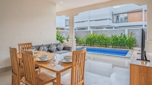 A dining area with a pool view, wooden furniture, and a modern interior design. - Aruna Villa 2 by Betterplace (Canggu)