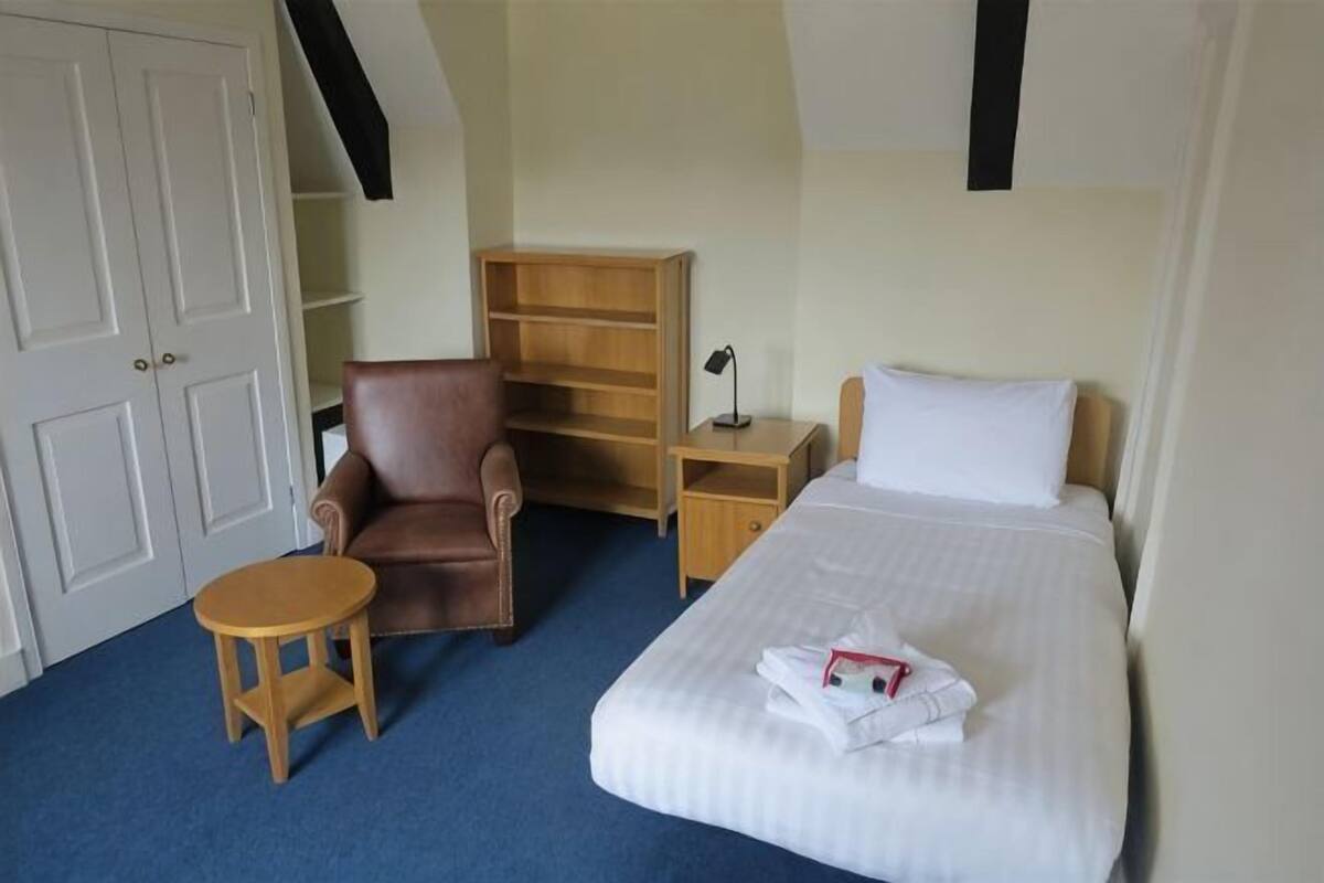 A hotel room with a bed, a chair, a small table, a nightstand, and a wardrobe.