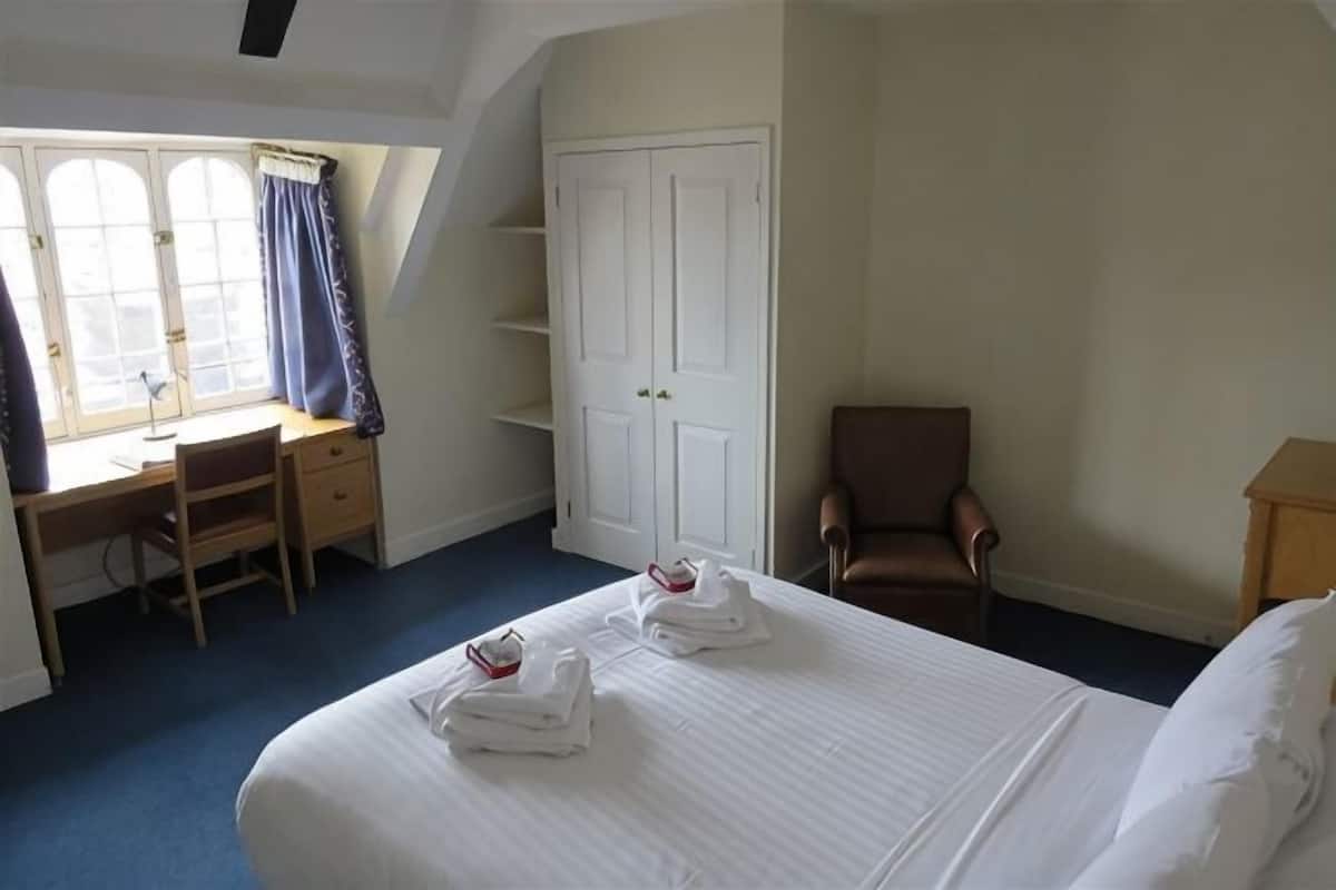 A hotel room with a bed, a desk, a chair, a wardrobe, and a window with curtains.