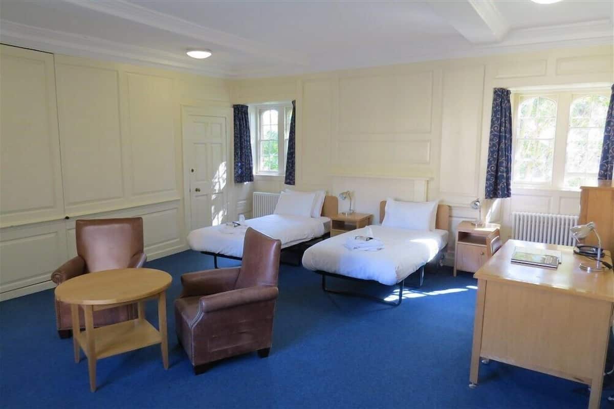 A hotel room with two single beds, a wooden desk, a chair, and a small round table.