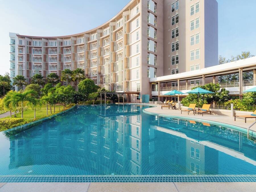 A hotel with a swimming pool, sun loungers, and a covered area with umbrellas.