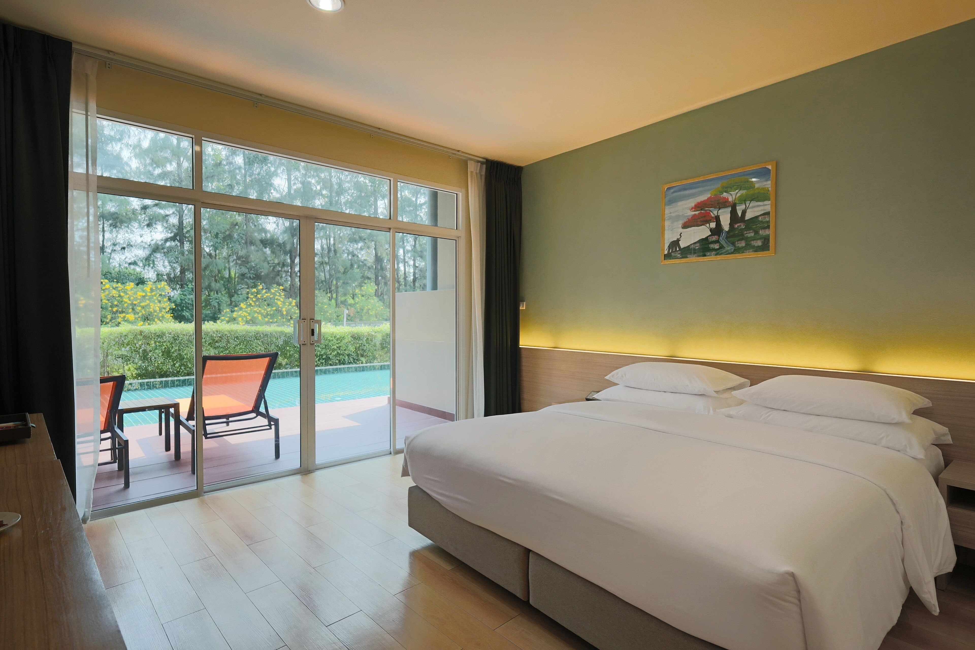 A hotel room with a large bed, a painting on the wall, and a view of a pool and greenery through the sliding doors.