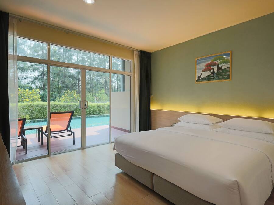 A hotel room with a large bed, a painting on the wall, and a view of a pool and greenery through the sliding doors.