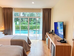 Hotelkamer met twee bedden, een televisie, een bureau met telefoon en uitzicht op een zwembad en groen.