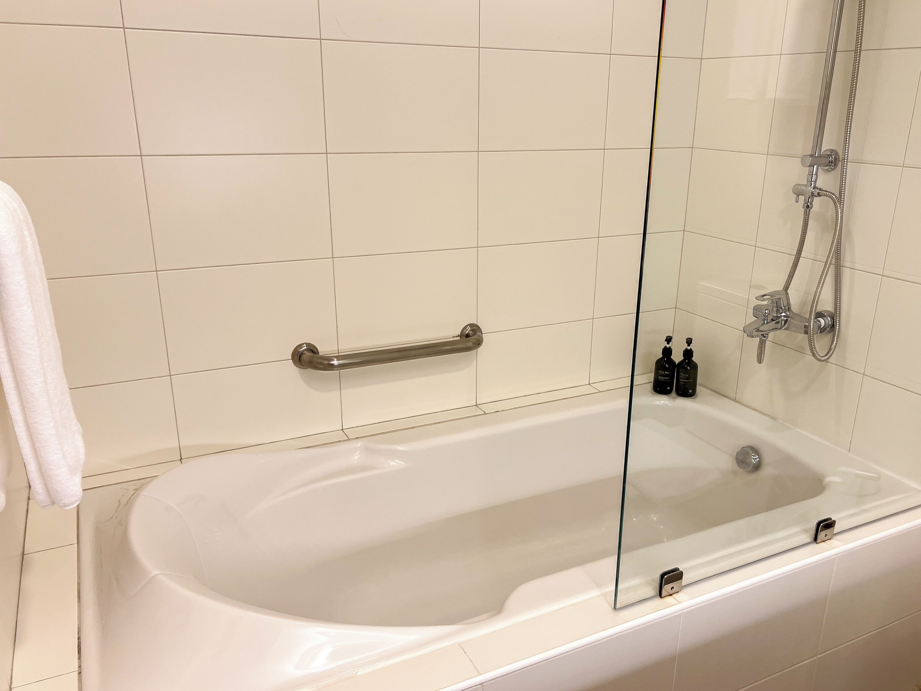 A modern bathroom with a bathtub, a glass shower enclosure, and a handrail.