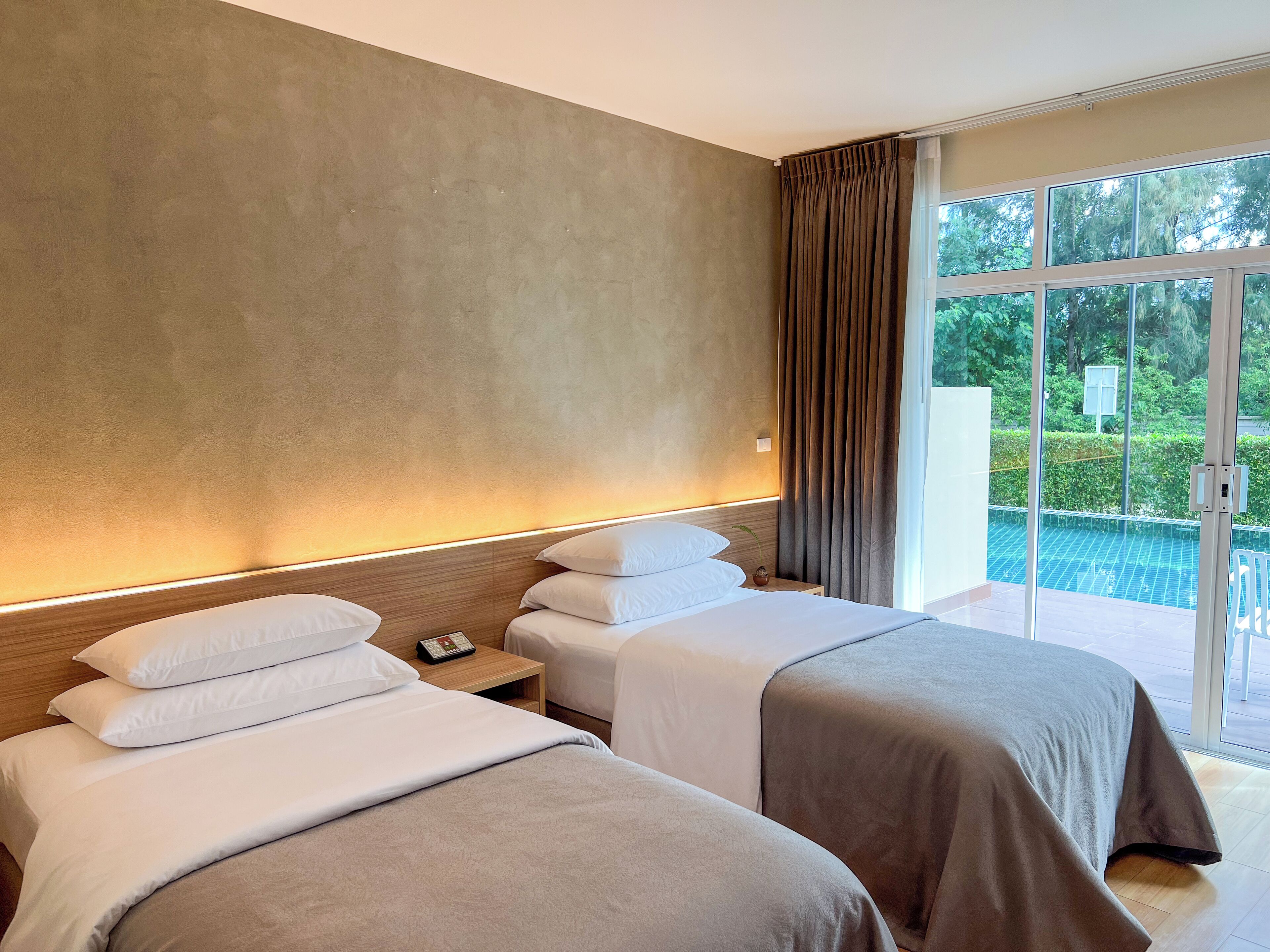 Une chambre d’hôtel avec deux lits, une table de chevet avec un téléphone et une vue sur une piscine, visible à travers de grandes fenêtres.