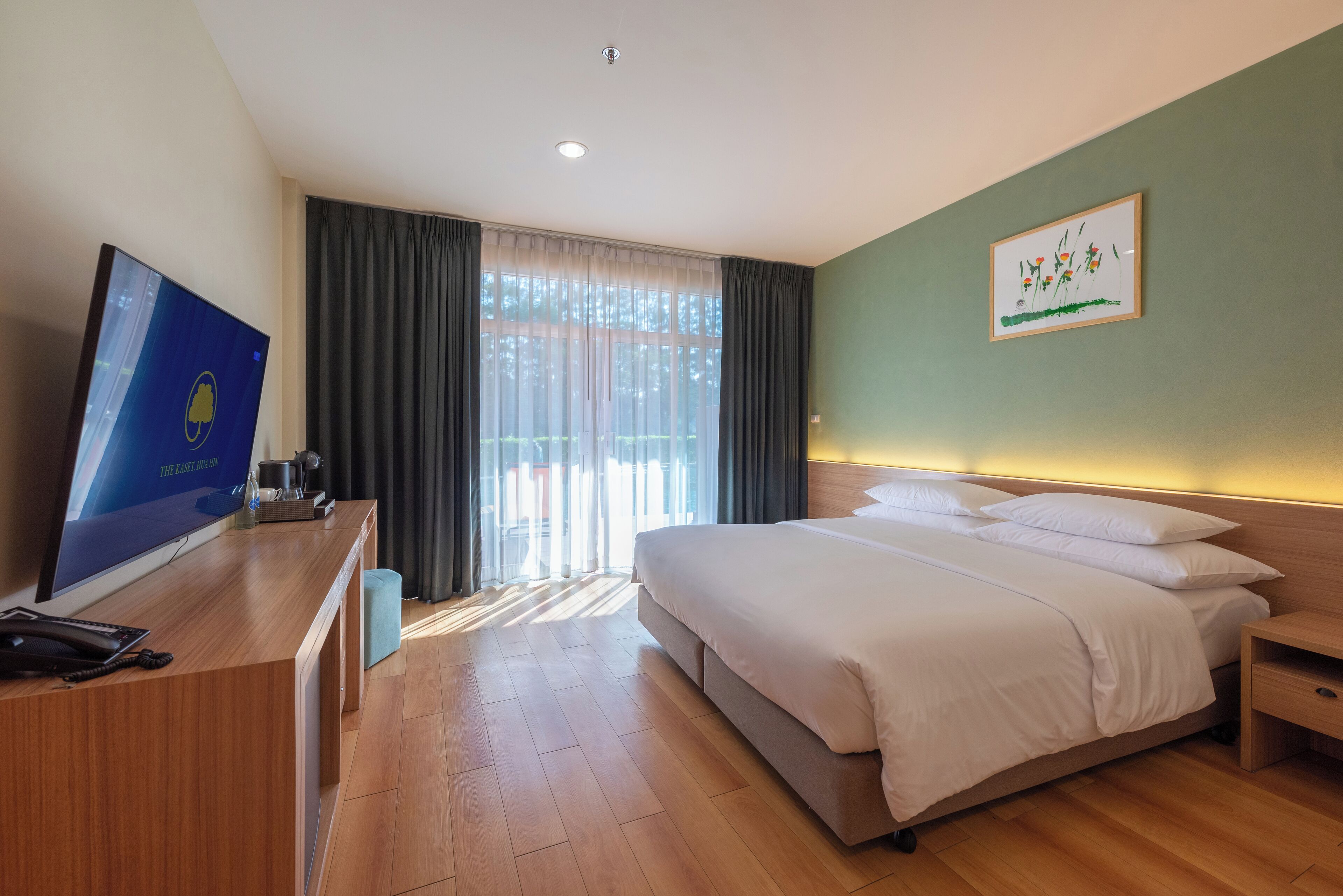 Habitación de hotel con cama, escritorio con monitor de computadora, teléfono y ventana con cortinas.
