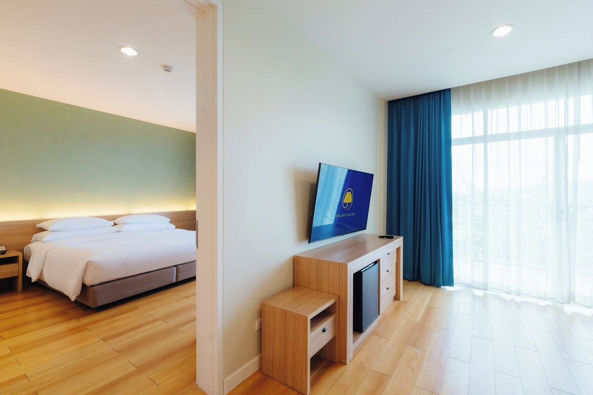 A hotel room with a bed, a TV, a desk, and a large window with curtains.