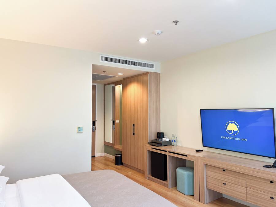 A hotel room with a bed, a TV on the wall, a desk with a computer, and a wardrobe.