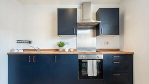 A modern kitchen with dark cabinetry, a stainless steel range hood, and a built-in oven. - Bright & Spacious 1 Bedroom Apartment in Bradford (Bradford)