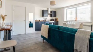 A modern living room with a teal sofa, a dining area, and a kitchen in the background. - Bright & Spacious 1 Bedroom Apartment in Bradford (Bradford)