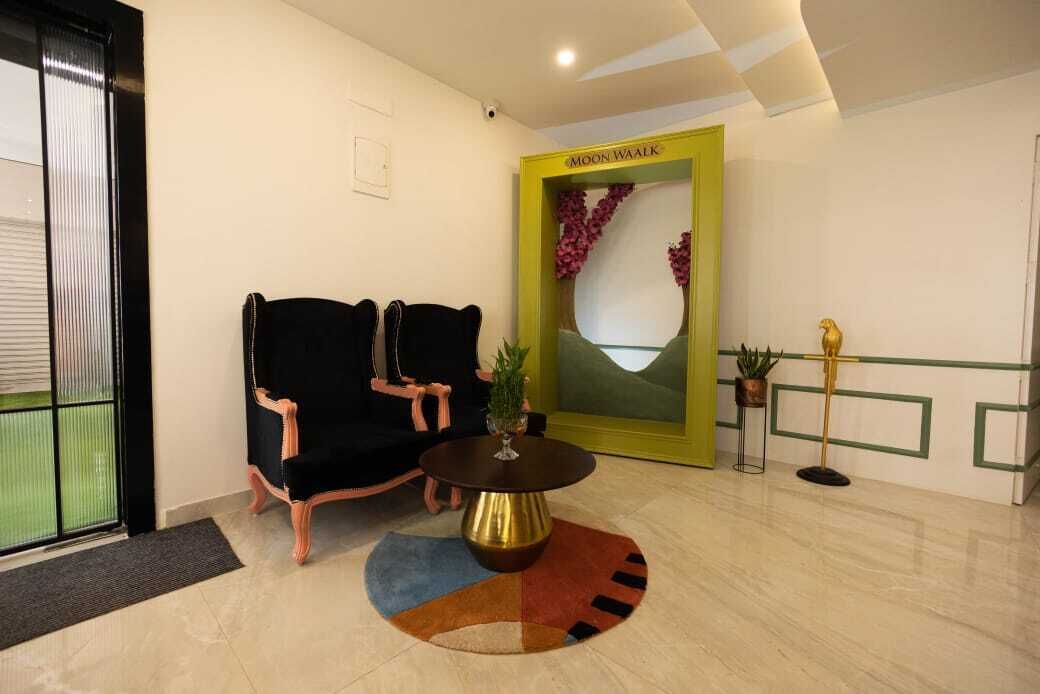 A reception area with a black sofa, a round table with a gold base, and a yellow-framed mirror.