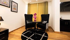 Une pièce avec une table ronde, deux chaises, un tapis noir et un rideau jaune.
