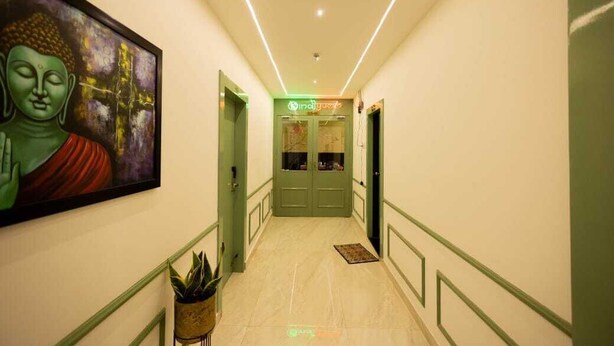 Un couloir orné d’un tableau représentant Bouddha, avec des portes vertes et une enseigne indiquant « Indy Hotel ».