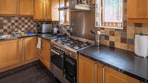 A modern kitchen with wooden cabinets, a gas stove, an oven, and a window with a view of greenery. - Luxurious Sheffield Villa With Stunning Views (Sheffield)