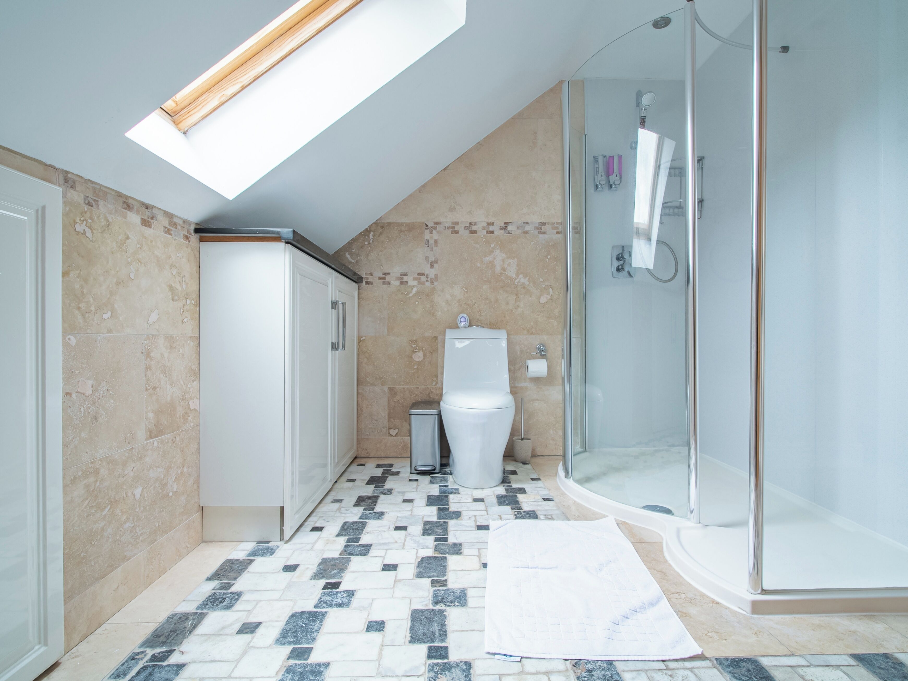A bathroom with a skylight, a shower, a toilet, and a tiled floor.