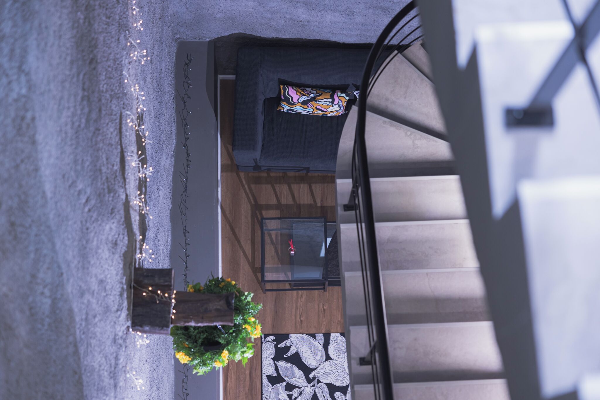 Ein modernes Interieur mit Holzboden, einem Glastisch und einem dunklen Sofa mit farbenfrohem Kissen.