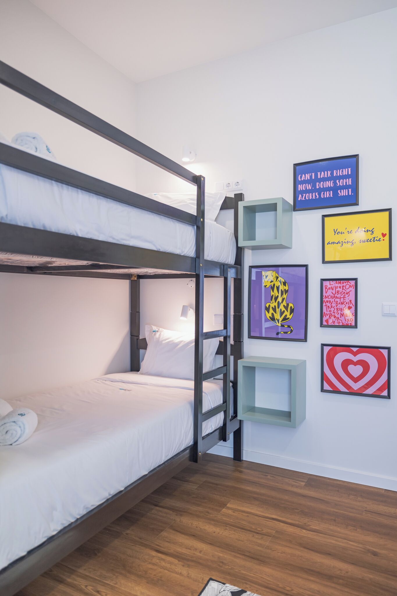 A bunk bed room with a ladder, a small shelf, and several framed pictures on the wall.