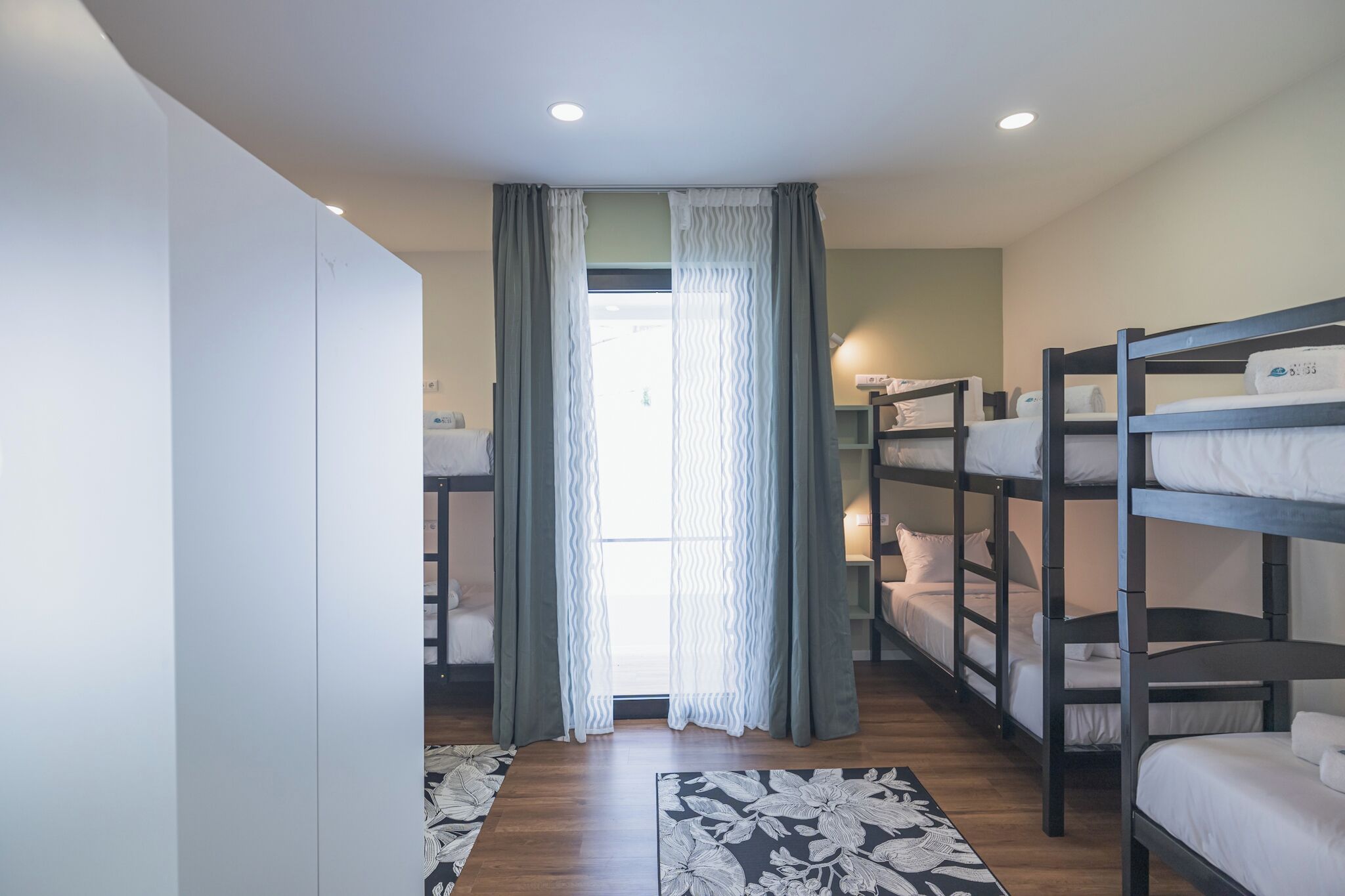 A room with bunk beds, a wardrobe, a patterned rug, and a window with curtains.