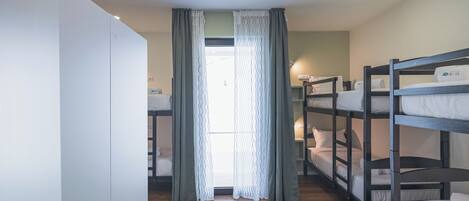 A room with bunk beds, a wardrobe, a patterned rug, and a window with curtains.