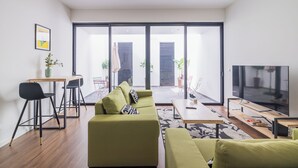 A modern living room with a green sofa, a dining area with a table and chairs, and a large TV.