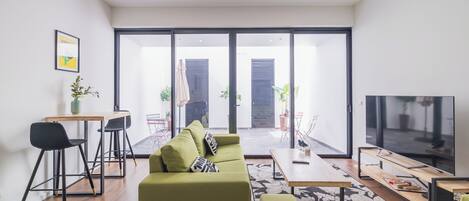 A modern living room with a green sofa, a dining area with a table and chairs, and a large TV.