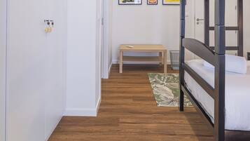 A bunk bed room with a wooden floor, a bench, and a small table.