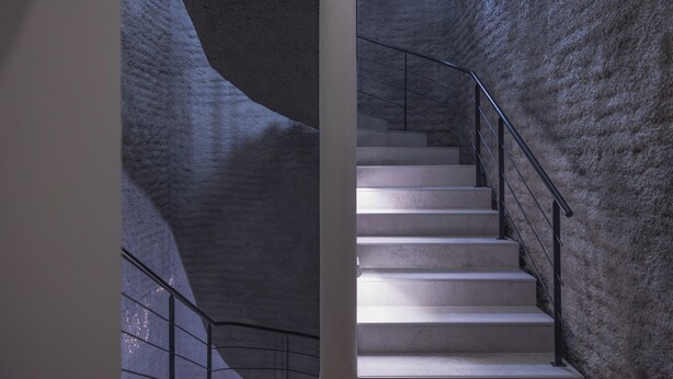 A staircase with a metal railing and a textured wall.