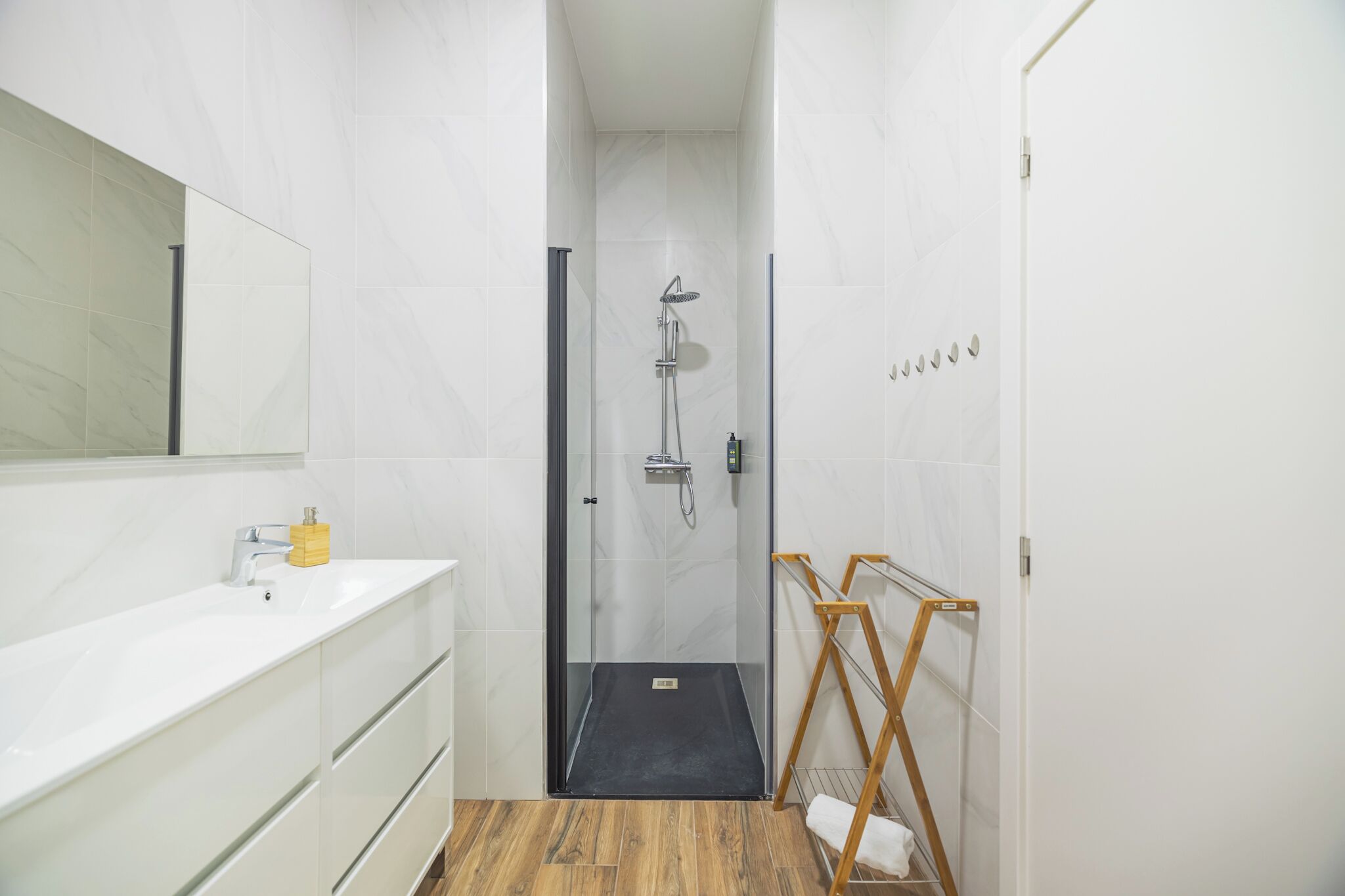 Ein modernes Badezimmer mit einer Duschkabine aus Glas, einem weißen Waschbecken mit gelbem Seifenspender und einem Holzboden.