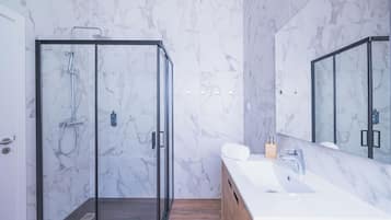 A modern bathroom with a glass-enclosed shower, a white marble wall, and a wooden vanity with a sink.