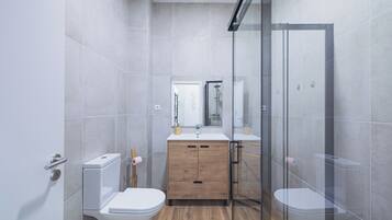 A modern bathroom with a glass shower enclosure, a wooden vanity, and a white toilet.