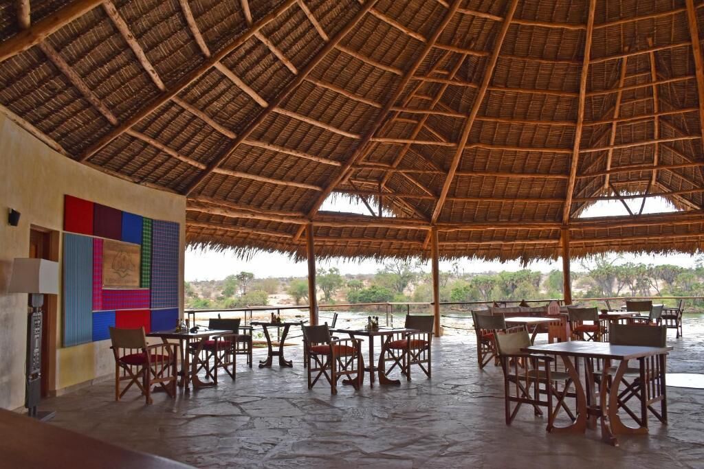 An open-air dining area with thatched roof and tables and chairs.