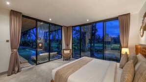 Ein Schlafzimmer mit einem großen Bett, Blick auf einen Swimmingpool und einem Stuhl am Fenster.