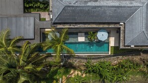 Ein modernes Haus mit Schwimmbad, umgeben von üppiger Vegetation und Palmen.