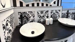 A bathroom with a black and white striped wall, a large mirror above a double sink, and a black countertop.