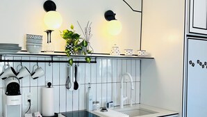 A modern kitchen with white cabinetry, a black countertop, a built-in oven, a kettle, and a coffee machine.