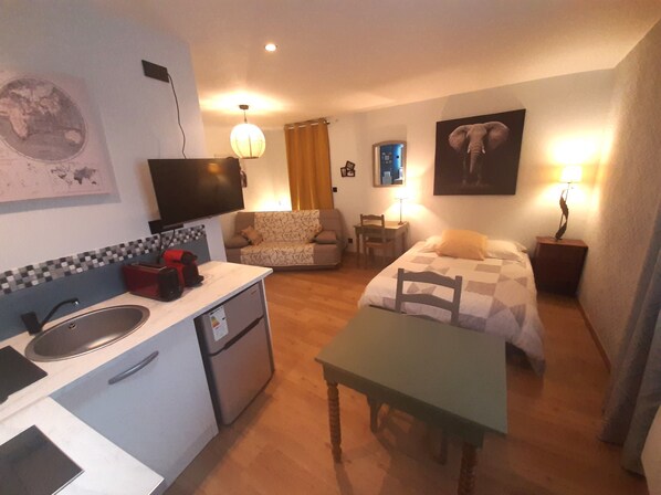 Een compacte hotelkamer met kitchenette, een bed, een bank, een bureau en een televisie.