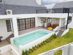 A modern house with a swimming pool, a dining area, and a staircase leading to an upper level.